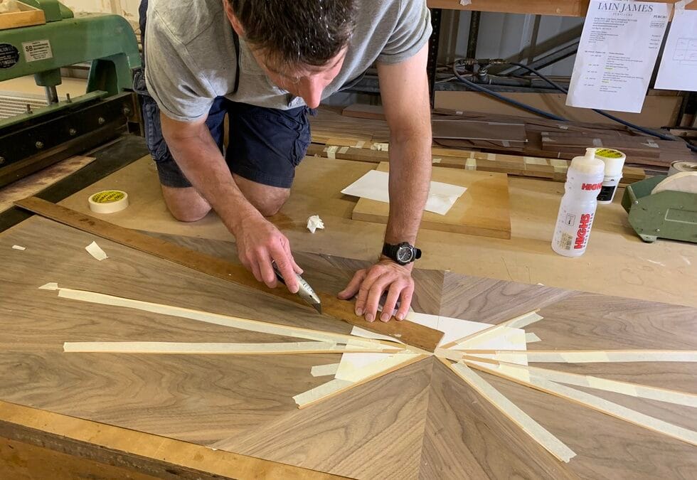 A craftsman in the Alden Cabinet Designs workshop carefully cuts and trims a radial wood veneer pattern for a bespoke table top.