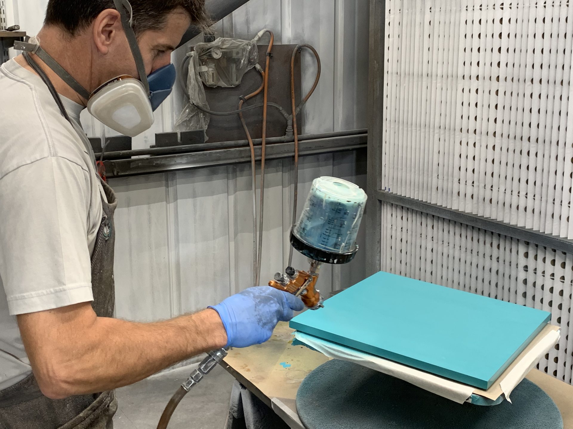 Craftsman spray-finishing a cabinet panel in workshop for bespoke furniture production